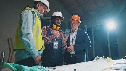 Builders and asian engineer, architect in safety helmets use smartphone and laughing relaxing during short break on construction site in building. Slow motion
