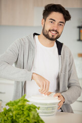young man spinning lettuce in plastic bowl