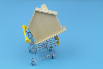 Purchase house concept. Shopping cart with wooden house on blue background.