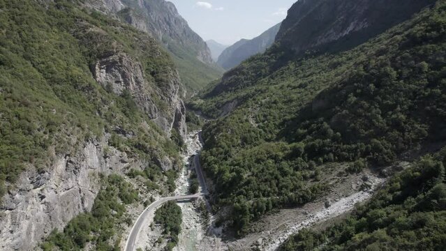 Frontal drone video moving between the hills of the valbone valley and over the Azem Hajdariy road and the river. The beauty of the landscape and a bird's-eye view of the bridge can be appreciated.