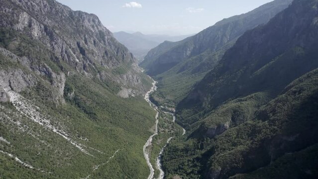 Frontal drone video moving between the hills of the valbone valley and over the Azem Hajdari road and the river. The beauty of the landscape can be appreciated from a bird's eye view.