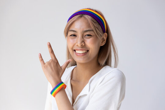 Happy LGBT woman wearing LGBTQ rainbow headband showing love hand sign, concept of gay pride month, lesbian pride, LGBT awareness movement, non-binary inclusivity and diversity