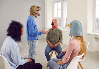 People wearing funny masks having a conversation during a group therapy session. Different male and female patients with animal faces talking, sharing their problems, and looking for solutions - obrazy, fototapety, plakaty