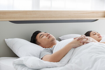 Closeup shot of Asian tired exhausted relaxing resting sleepy female housewife laying down on pillow cover with white soft blanket sleeping has sweet dream on bed in bedroom beside male husband