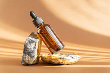 Serum in glass amber bottle with dropper lid on stand made of natural granite stone. Essential oil...