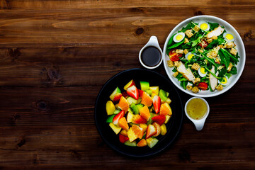 Top view shot of delicious healthy appetizers mixed sliced fresh raw fruits strawberry kiwi and green vegetables with boiled eggs salad dishes and dressing sauce placed on old vintage wooden table
