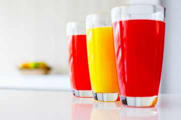Closeup shot of three tall round glasses of red and yellow cold healthy tasty mixed fresh raw vegetables and fruits juice cocktail soft drink placed on table with copy space and blurred background
