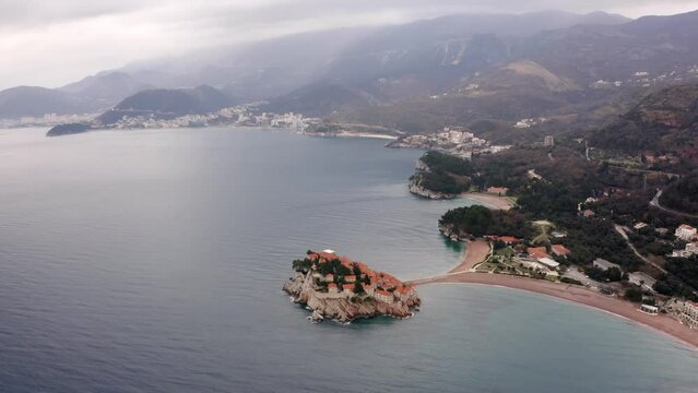 AERIAL - Sveti Stefan island, tombolo, and Villa Milocer in Montenegro, reverse