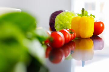 Closeup shot of red fresh raw delicious tasty organic tomatoes with shadow reflection on kitchen counter table placed together with yellow sweet pepper green cabbage and lettuce in blurred background