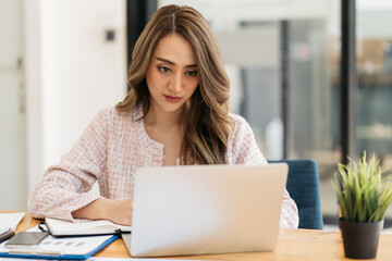 Happy attractive Asian business woman working with a laptop and financial document at office, successful action, Business concept.