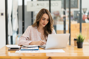 Happy attractive Asian business woman working with a laptop and financial document at office, successful action, Business concept.