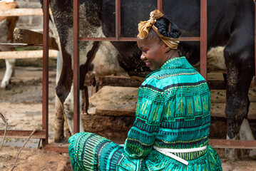 Young African woman seated next to cow shed 