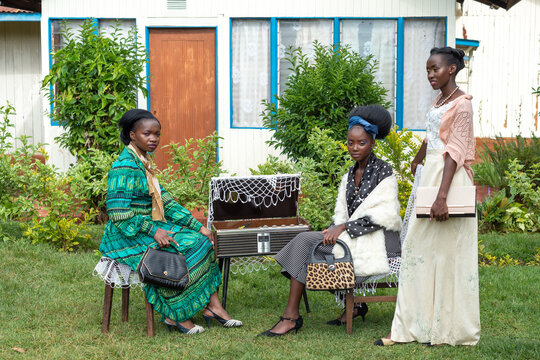 Three young african women posing with an old record player  in front of rural house 