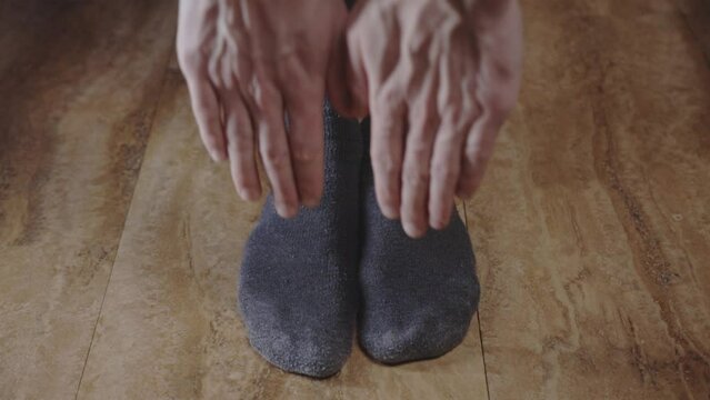 Man Wearing Gray Socks Standing With Feet Flat On Wooden Floor, Stretching And Reaching Toes With Both Hands.  - Low-Level Shot