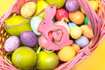 Colorful Easter eggs and a bunny in a Easter basket on a yellow background, top view, close up. Easter holiday concept.