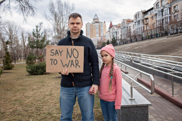 Middle aged father with his daughter holding a poster with anti-war message over cityscape...