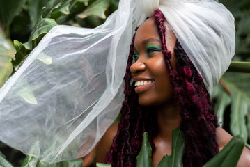 Portrait of a smiling young African woman, in leaves, wearing a  headwrap - obrazy, fototapety, plakaty