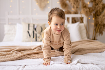 Fototapeta premium a small child on a bed in beige brown natural tones is laughing and rejoicing, a cheerful and funny little kid is playing at home