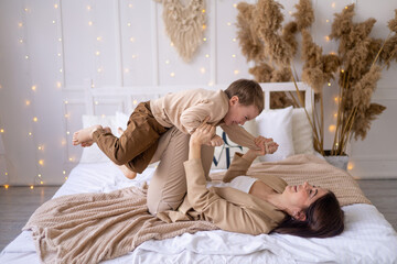 mom and a little boy play, cuddle and make a plane at home on a bed in natural brown tones, a happy family with a small child has fun together