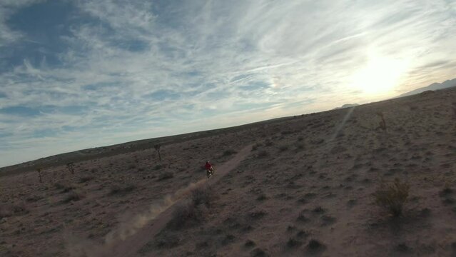 Drone following a speeding motorcyclist riding along a dusty trail in the Mojave Desert at sunset
