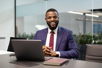 Fototapeta na wymiar Cheerful black businessman posing at workdesk in office