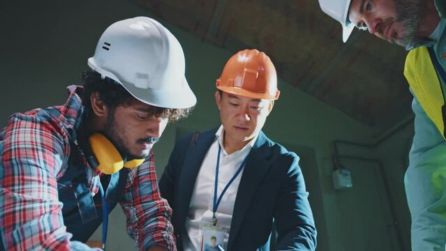 Asian architect and builders engineers with in hardhats and uniforms checking, drawing on blueprint talking about construction project in the evening light during renovation in building Slow motion