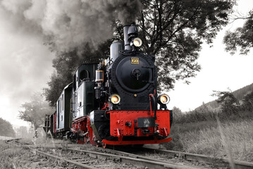Naklejka premium Historic steam train on a narrow gauge railway track in Sauerland Germany is a tourist attraction. Locomotive with coaches and smoking engine in black and white vintage with colored elements. 