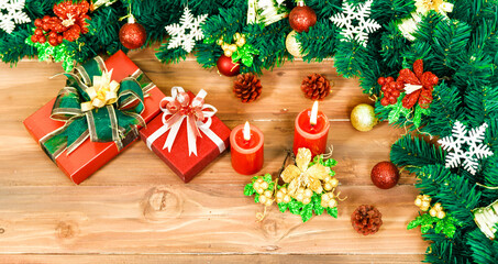 Closeup studio shot of Red paper wrapped present gift boxes with ribbon bowtie candles and wreath placed on wood floor decorated with Christmas eve pine tree with sphere balls snowflakes hanging