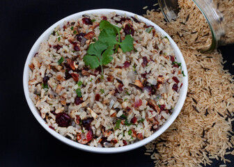 Delicious and healthy Wild rice pilaf with cranberries and pecan nuts on black surface with raw...