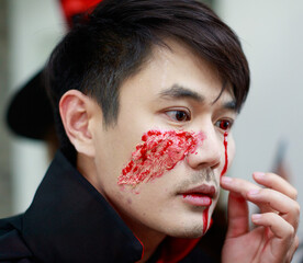 Closeup shot of Asian young handsome male model face wearing scary creepy makeup with red bloody...