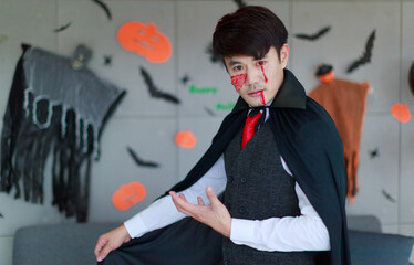 Portrait studio shot of Asian young male model in scary vampire costume with rope wearing blood makeup look at camera posing in full decorated living room for traditional festival Halloween party
