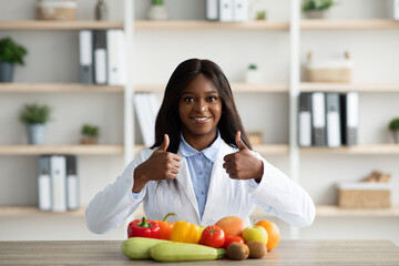 Young african american female nutritionist recommending eating fruits and vegetables, showing thumbs up