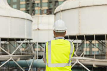 Asian engineer man or architect looking forward with white safety helmet in city construction site . Standing on rooftop building construction at capital.