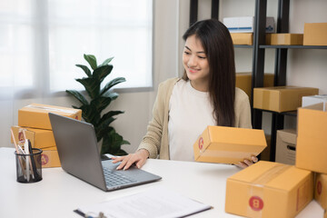 Young asian entrepreneur woman checking product on stock take note with laptop. Business woman working SME online at home. Check address on parcel. Small business owner start up freelance concept.