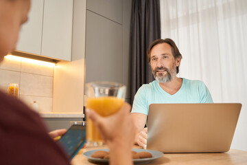 Daughter using mobile and drinking juice while her father looks at her