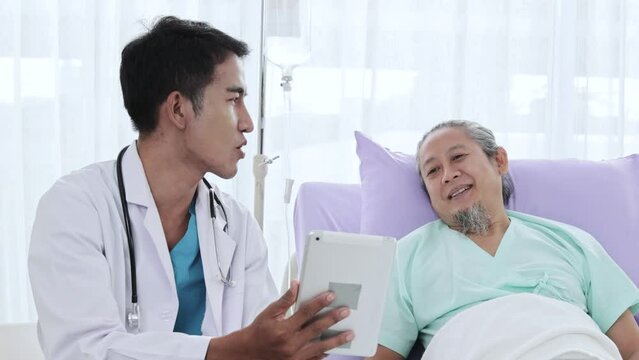 young asian man doctor uses digital tablet during consultation with senior man in hospital