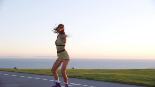 Cheerful, smiling caucasian woman riding rollers in front of the camera. Wonderful professional dance of a girl in green top and shorts with a sunset behind. High quality 4k footage