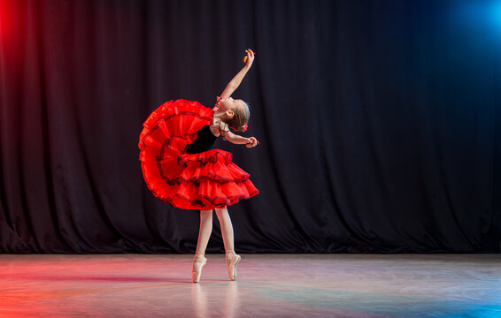 A little girl ballerina is dancing on stage in a tutu on pointe shoes with castanedas, the classic variation of Kitri.