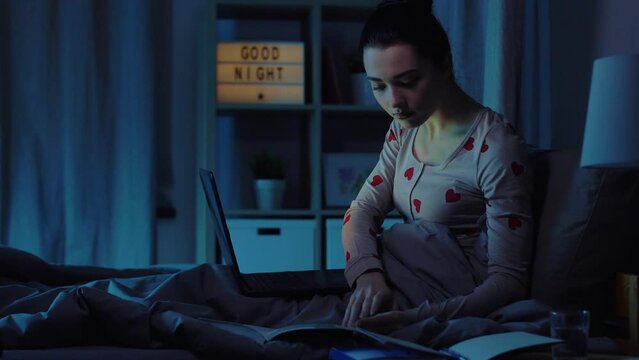 education, technology and people concept - teenage student girl with laptop computer and books learning in bed at home at night