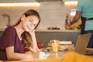 Teenager studying at kitchen table next to her parent