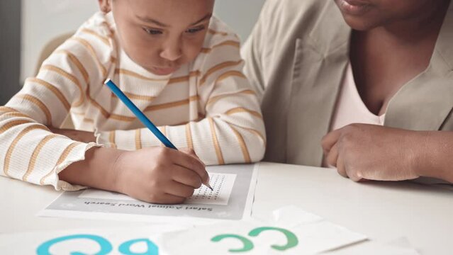 Medium closeup with slowmo of smart 5 year old African-American girl studying English alphabet together with female teacher at desk in classroom
