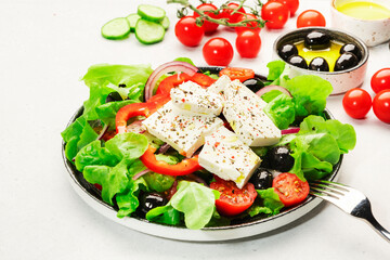 Greek salad with feta cheese, olives, cherry tomato, paprika, cucumber and red onion, healthy vegeterian mediterranean diet food, low calories eating. White stone background, top view