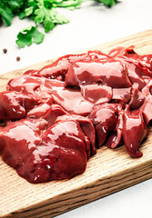 Fresh raw chicken liver on cutting board and ingredients for cooking on concrete white stone kitchen table, top view, copy space