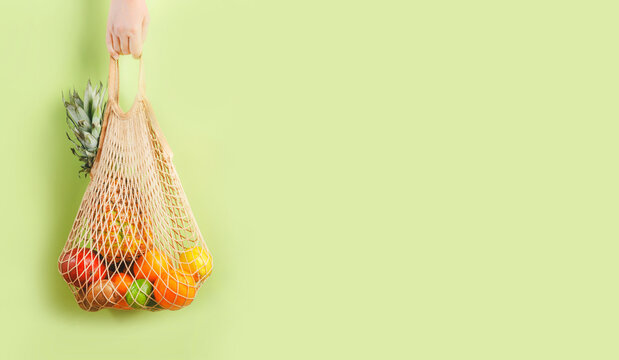 Woman hand holding eco friendly shopping bag with various tropical fruits on green banner background. Sustainable lifestyle. Plastic free. Zero waste concept