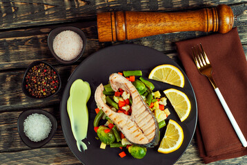 Fototapeta na wymiar Grilled salmon steak. Red salmon with lemon and vegetables close up. wasps on a salad of boiled cabbage, carrots, green peas and broccoli. Food on shabby wooden table.