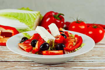 Salad of cabbage, tomato, pepper, olives and cheese in a white plate. Greek salad close up on a background of fresh vegetables.