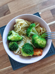 Plate with simple healthy food - spaghetti pasta, broccoli, chicken on a wooden table. Lunch or dinner in an ordinary family, authentic photo, flat lay