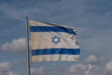 A large, blue and white flag of the State of Israel rippling in the wind on a sunny day during the national observance of the Independence and Memorial day holidays.