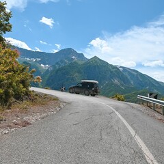 Geländewagen mit Dachzelt steht an einer Passstraße mit Blick auf Berge