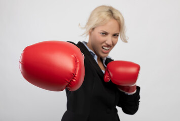 Young boxing businesswoman punching towards camera wearing red boxing gloves, selective focus,...